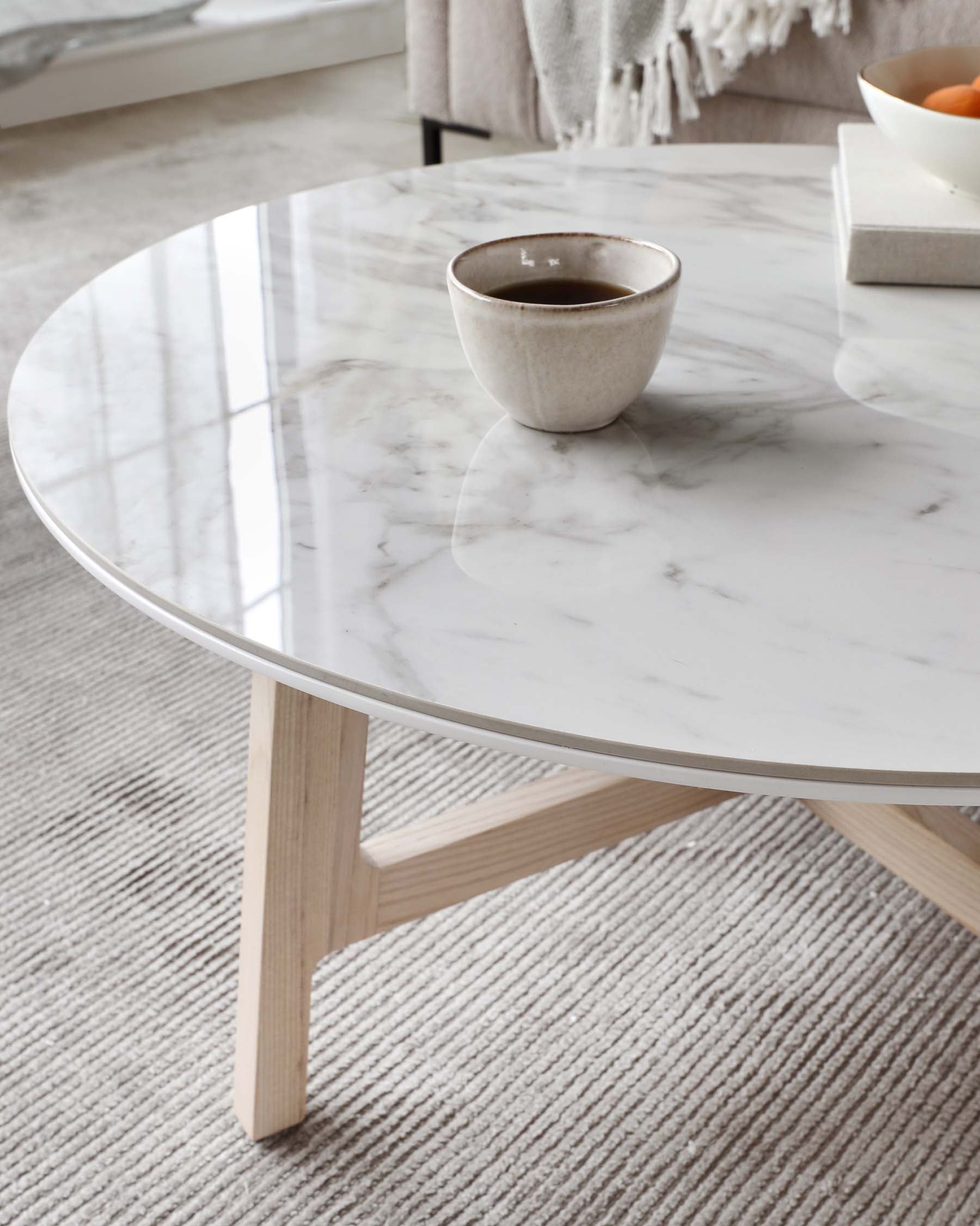 Round marble-top coffee table with light wooden legs displaying a minimalist aesthetic.