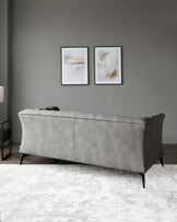 A modern, button-tufted sofa with a curved silhouette upholstered in a grey velvet fabric, featuring tapered black wooden legs, set in a minimalistic room with abstract wall art and a soft white area rug.