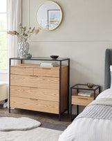 Modern bedroom furniture set featuring a natural wood-grain finish. A four-drawer dresser with slim, horizontal brass handles stands next to a simple, two-tiered nightstand with a black metal frame and wooden shelves. Both pieces have clean lines and a contemporary design aesthetic.