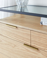 Modern light wood dresser with clean lines and minimalist handles under a glass console table displaying a ceramic vase.