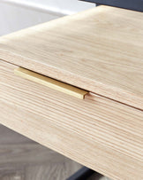 Close-up of a modern light wood drawer with a minimalist brass handle, showcasing fine wood grain texture and precise craftsmanship.