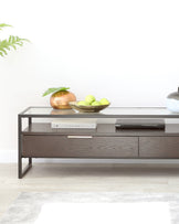 Modern minimalist-style coffee table featuring a clear glass top with a sturdy metal frame in a dark finish and a lower wooden shelf with two drawers for handy storage space.