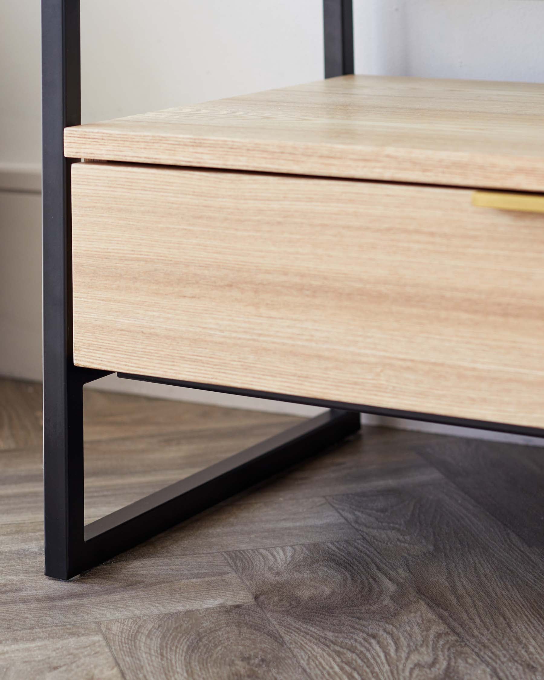 Close-up of a modern minimalist wooden drawer with a light oak finish and a sleek, black metal frame, featuring a slim brass handle.