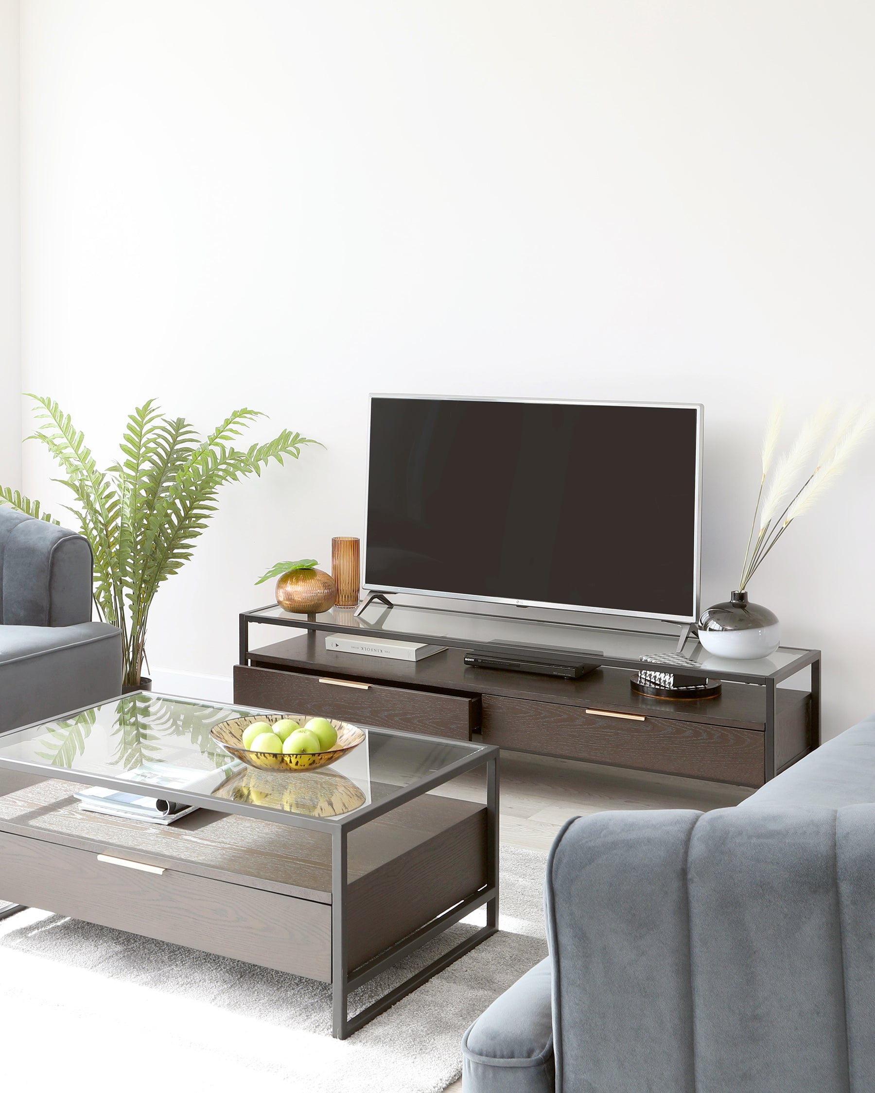 Modern living room furniture featuring a sleek dark wood and glass coffee table, complemented by a matching wood television stand with ample storage space. Flanked by two contemporary charcoal grey upholstered sofas with clean lines, the setup embodies a chic and minimalist aesthetic.