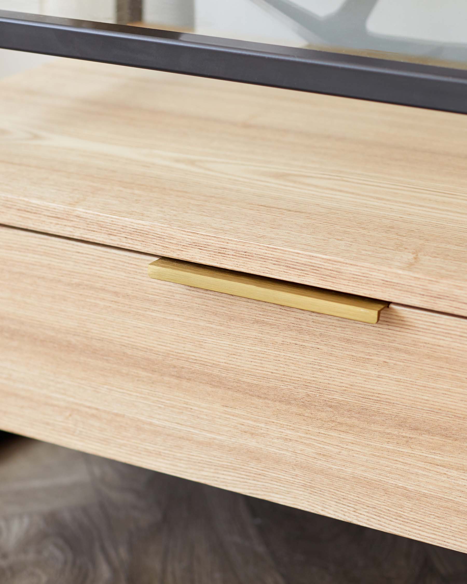 Light wood finish drawer front with a minimalist brass handle, indicating a modern and sleek design aesthetic.