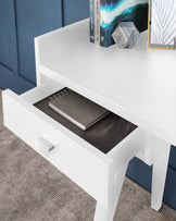 Modern white coffee table with a lower shelf and an open drawer displaying a notebook, complemented with decorative items on top.