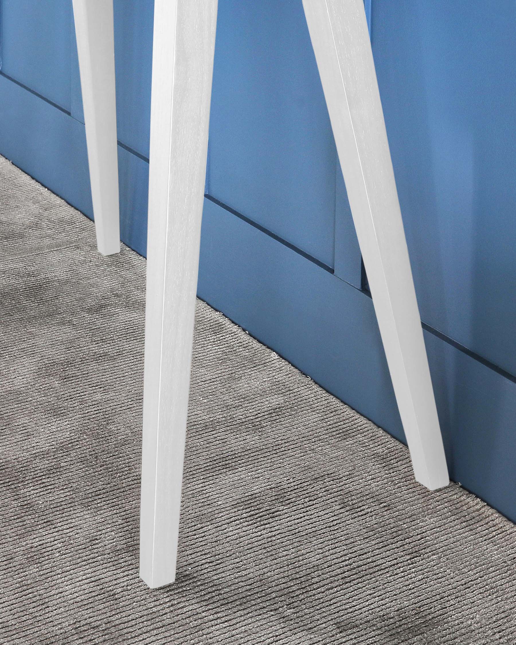 White modern chair legs with a sturdy and sleek design on a textured grey carpet. The background features a blue panelled wall, emphasizing a clean and contemporary aesthetic.