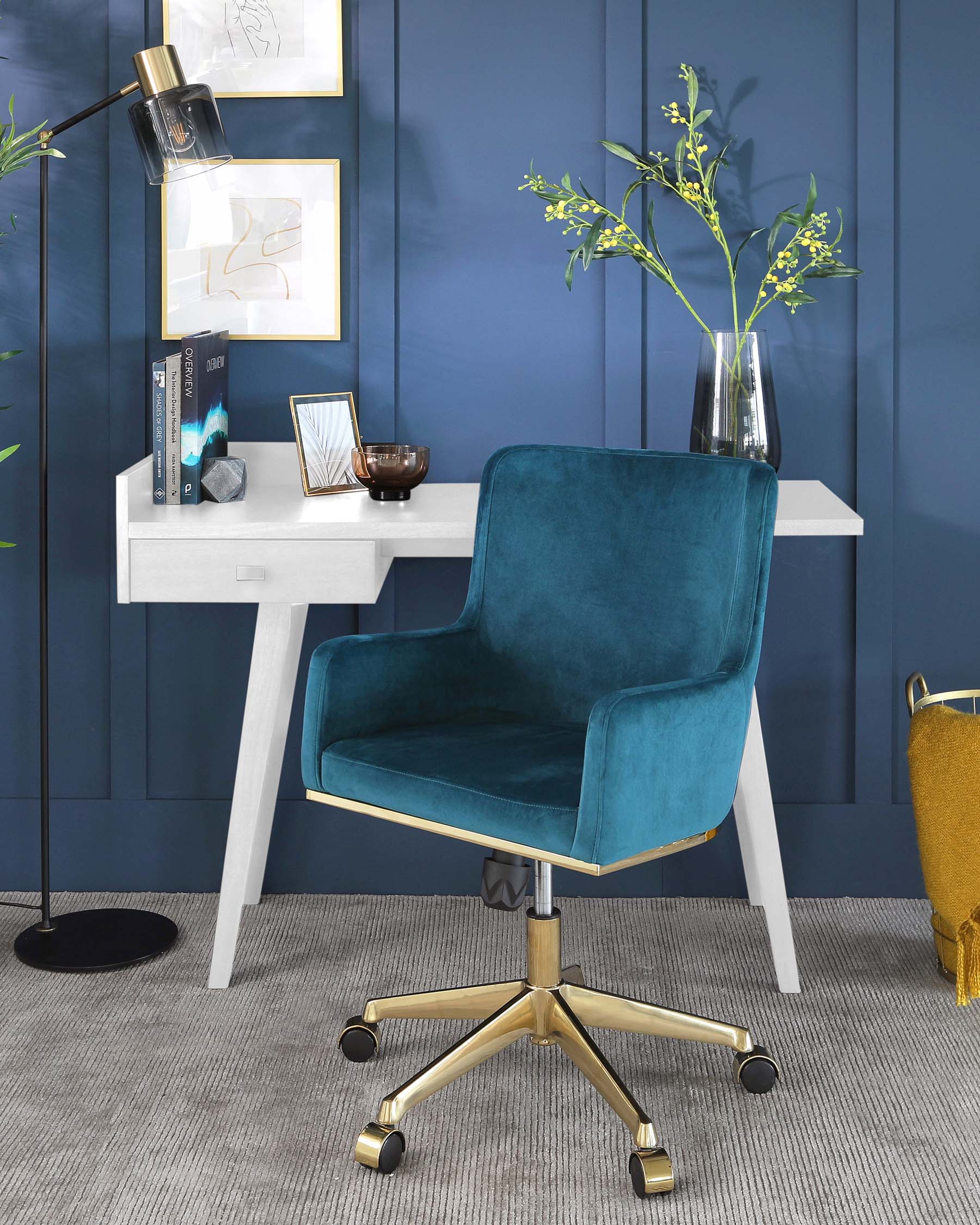 Elegant teal blue velvet office chair with a high back, armrests, and a gold metal base with caster wheels. Next to it is a simplistic white desk with clean lines.