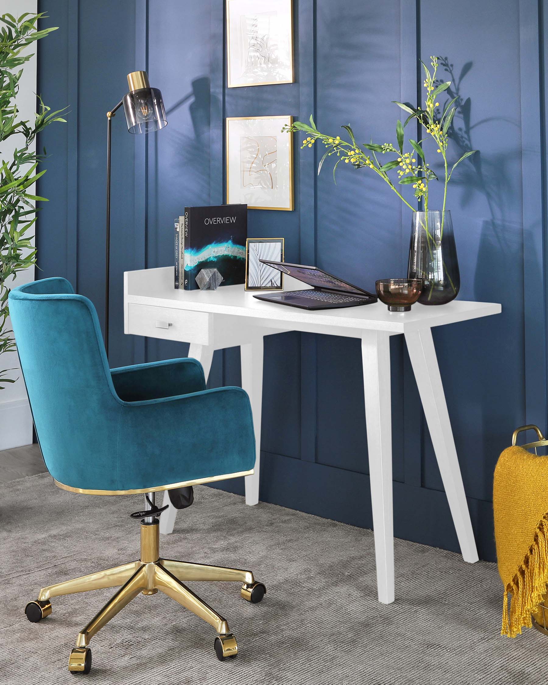 Modern workspace furniture featuring a streamlined white desk with A-frame legs paired with an elegant teal blue office chair. The chair has a high back, curved armrests, and a plush velvet fabric, complemented by a shiny gold swivel base with caster wheels.