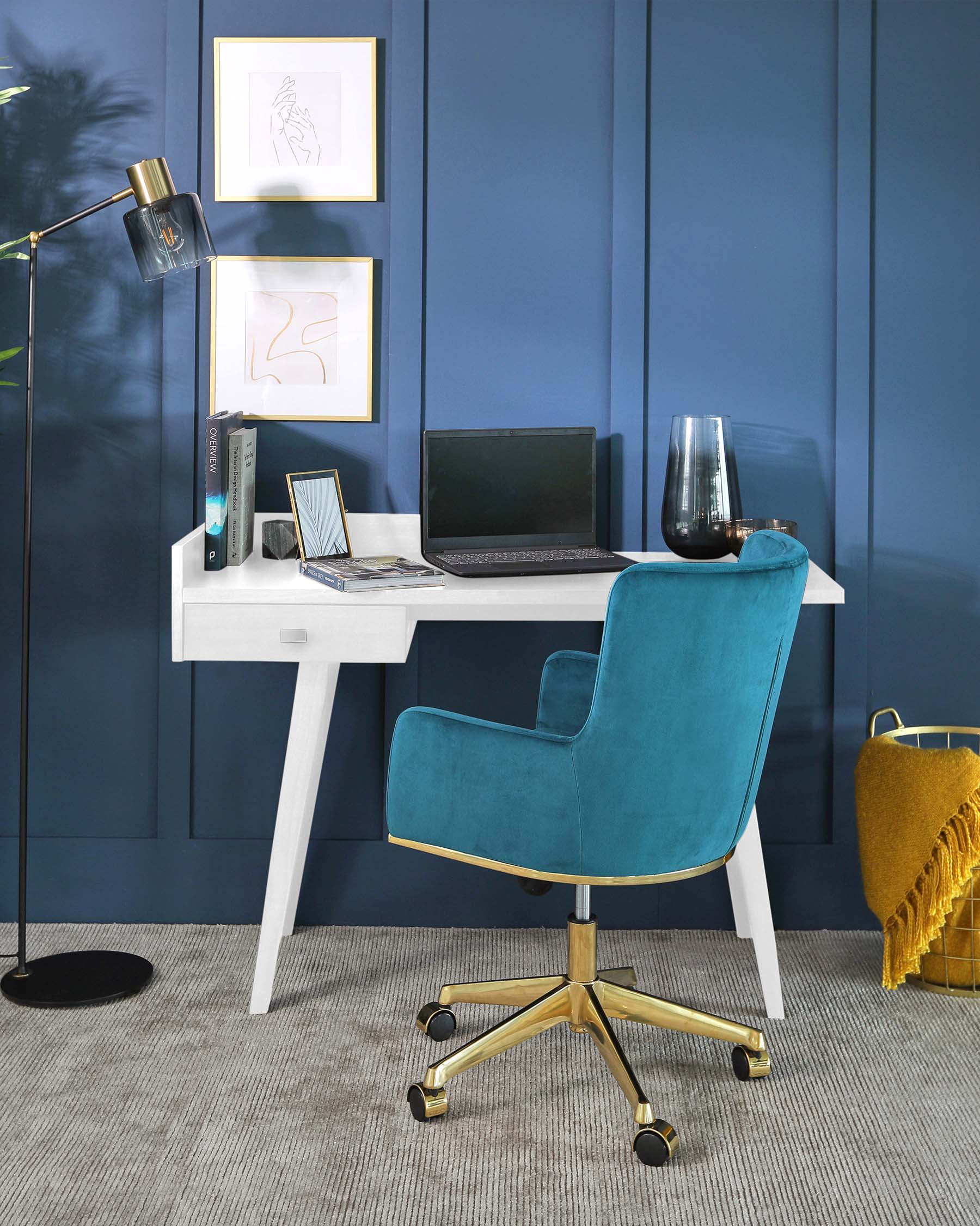 Contemporary workspace featuring a sleek white desk with clean lines and angled legs, paired with an elegant teal blue velvet office chair with a curved backrest and gold-finished metal base with caster wheels. The chair's luxurious fabric and colour contrast boldly against the rich blue panelled wall.