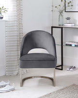 A modern velvet accent chair with a unique curved silhouette, featuring a plush round back and a comfortable seat cushion. The chair is supported by a stainless steel base with a brushed finish, adding to its contemporary appeal.