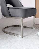 Modern sleek chair with a curved backrest and a cushioned seat, upholstered in grey velvet, supported by a metallic silver cantilever base.