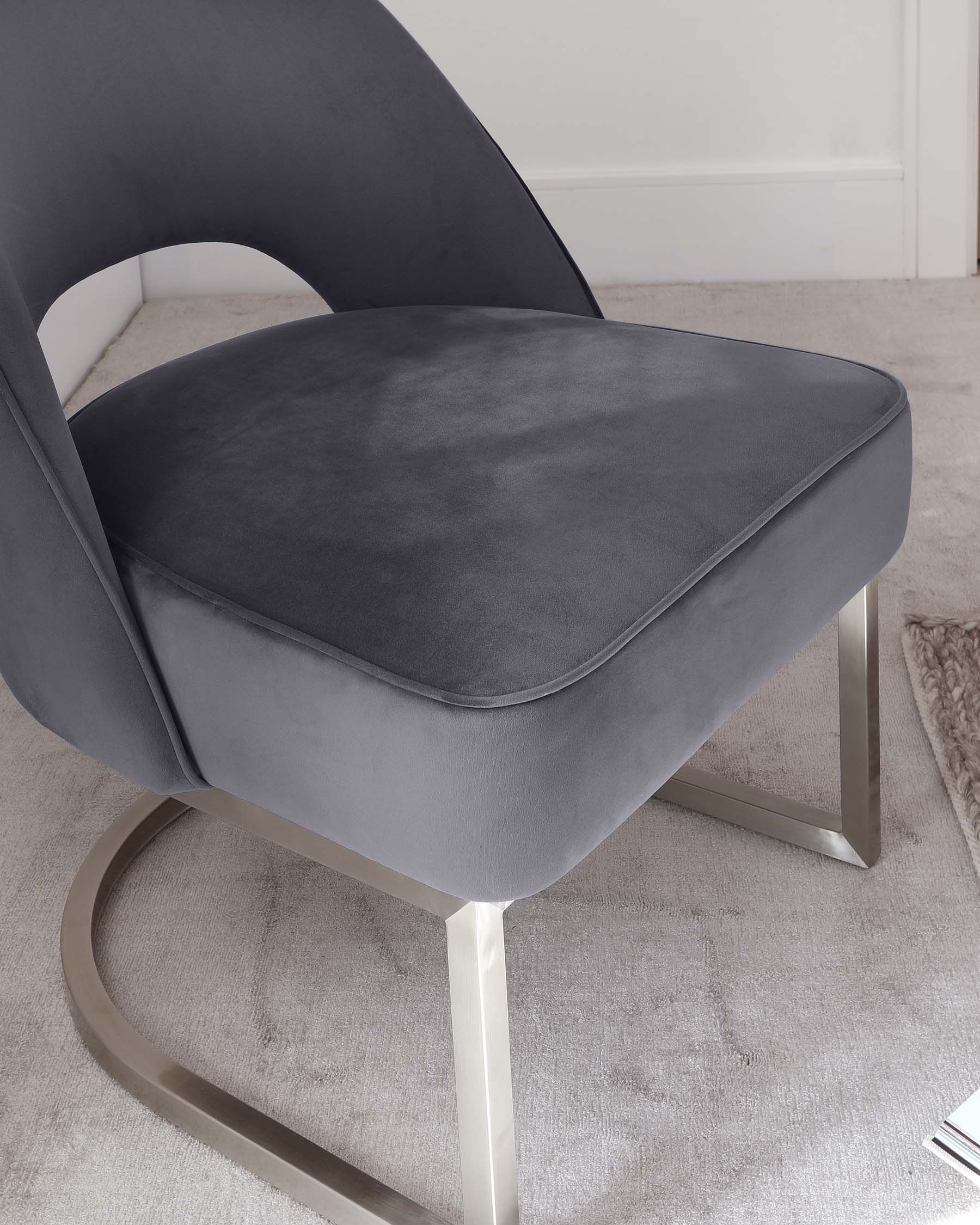 Contemporary grey velvet accent chair with a unique curved backrest and a thick, cushioned seat atop a smooth, polished metallic silver base in a sleek, geometric design.