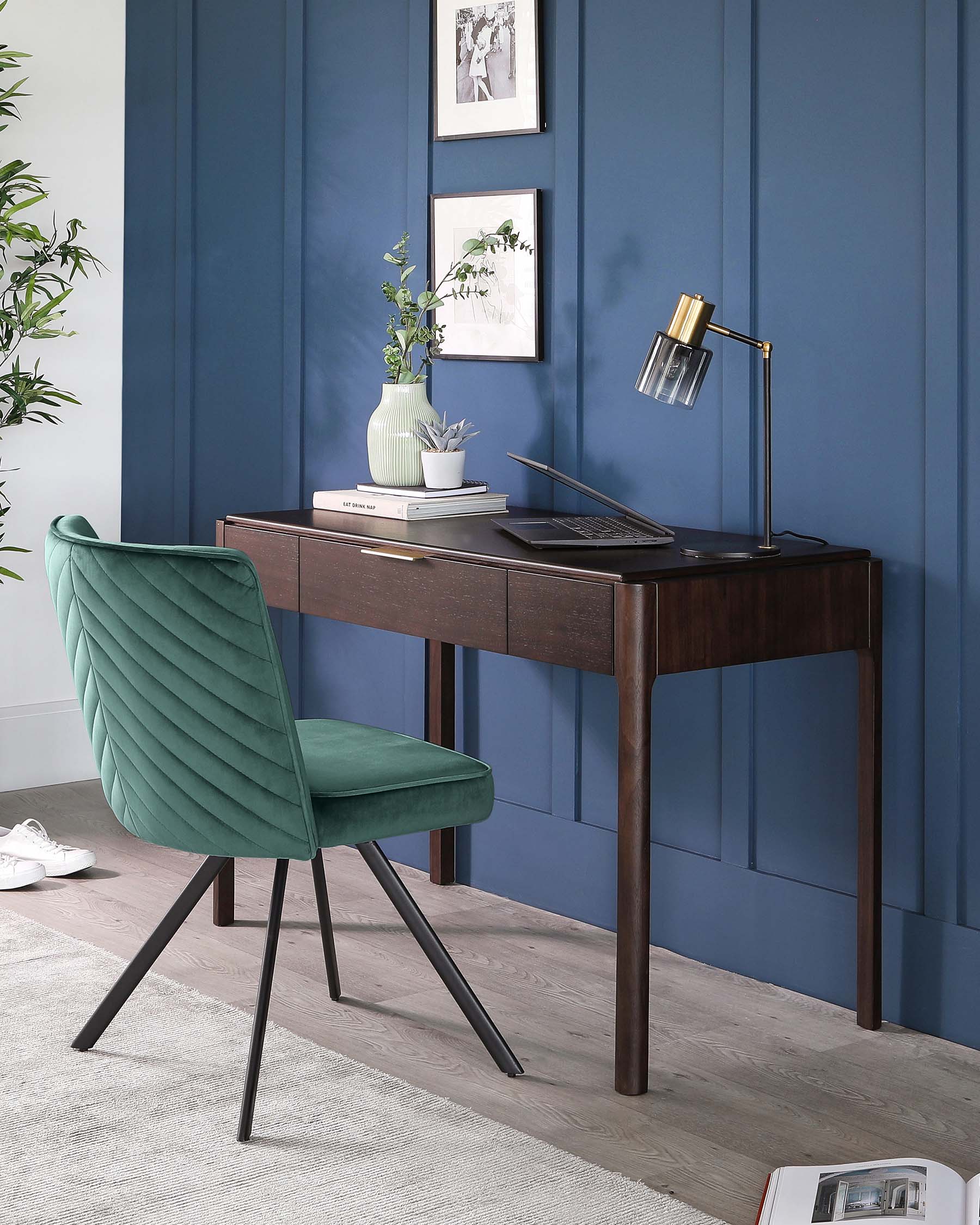 A sleek, dark wooden writing desk with tapered legs, featuring a slim drawer under the tabletop, paired with a modern green velvet chair that has a quilted backrest and angular black metal legs.