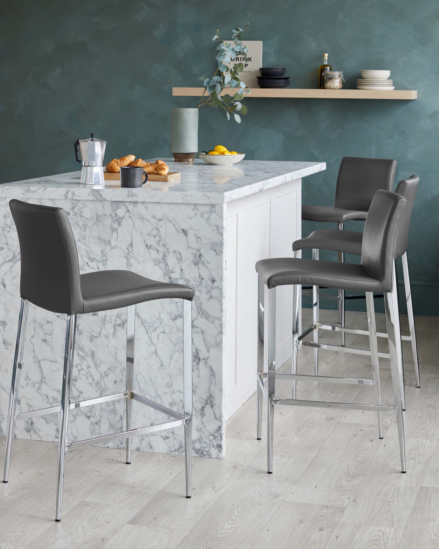 Elegant modern kitchen bar stools with grey upholstery and chrome leg design, positioned at a white marble countertop.