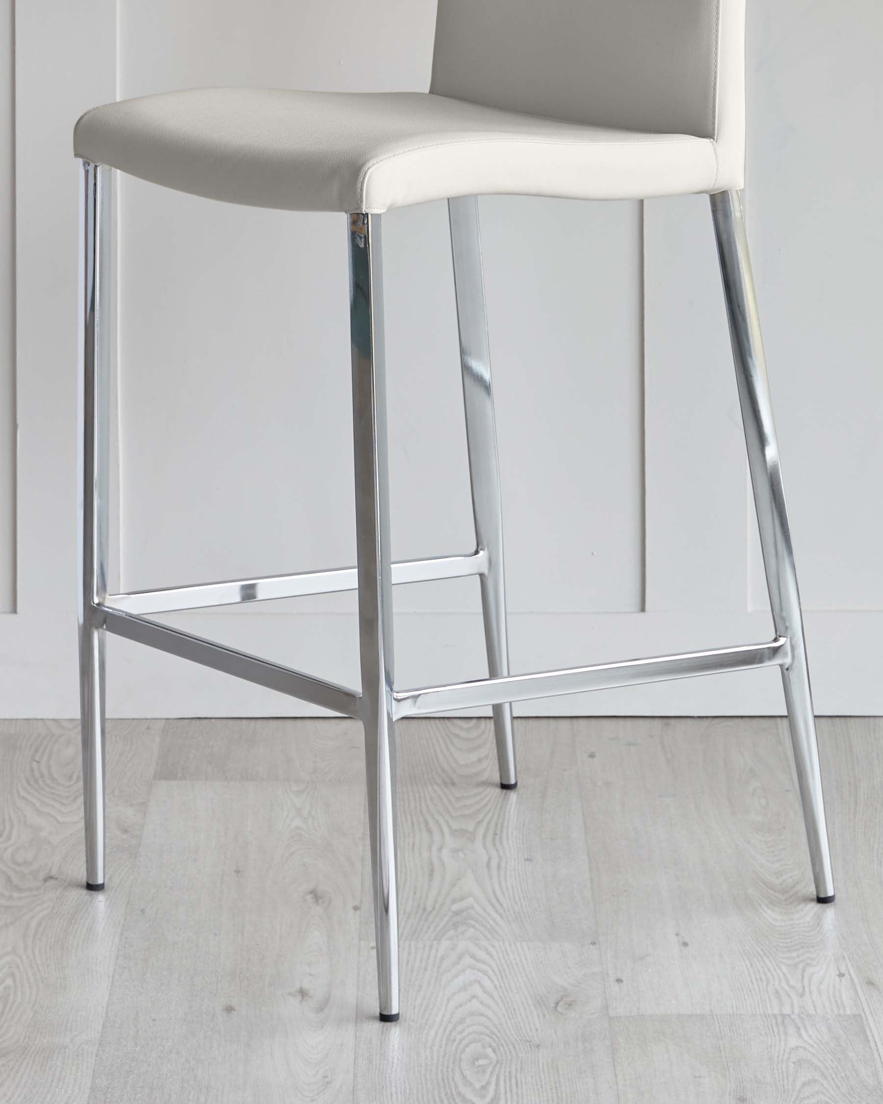 Modern bar stool with a chrome steel frame and a light taupe faux leather upholstered seat and backrest, set against a white wall on a light wooden floor.