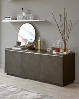 Modern dark wood sideboard with clean lines and handle-less design, featuring a wall-mounted white shelf above and accessorized with a circular mirror, decorative vases, and a selection of decanters on top.