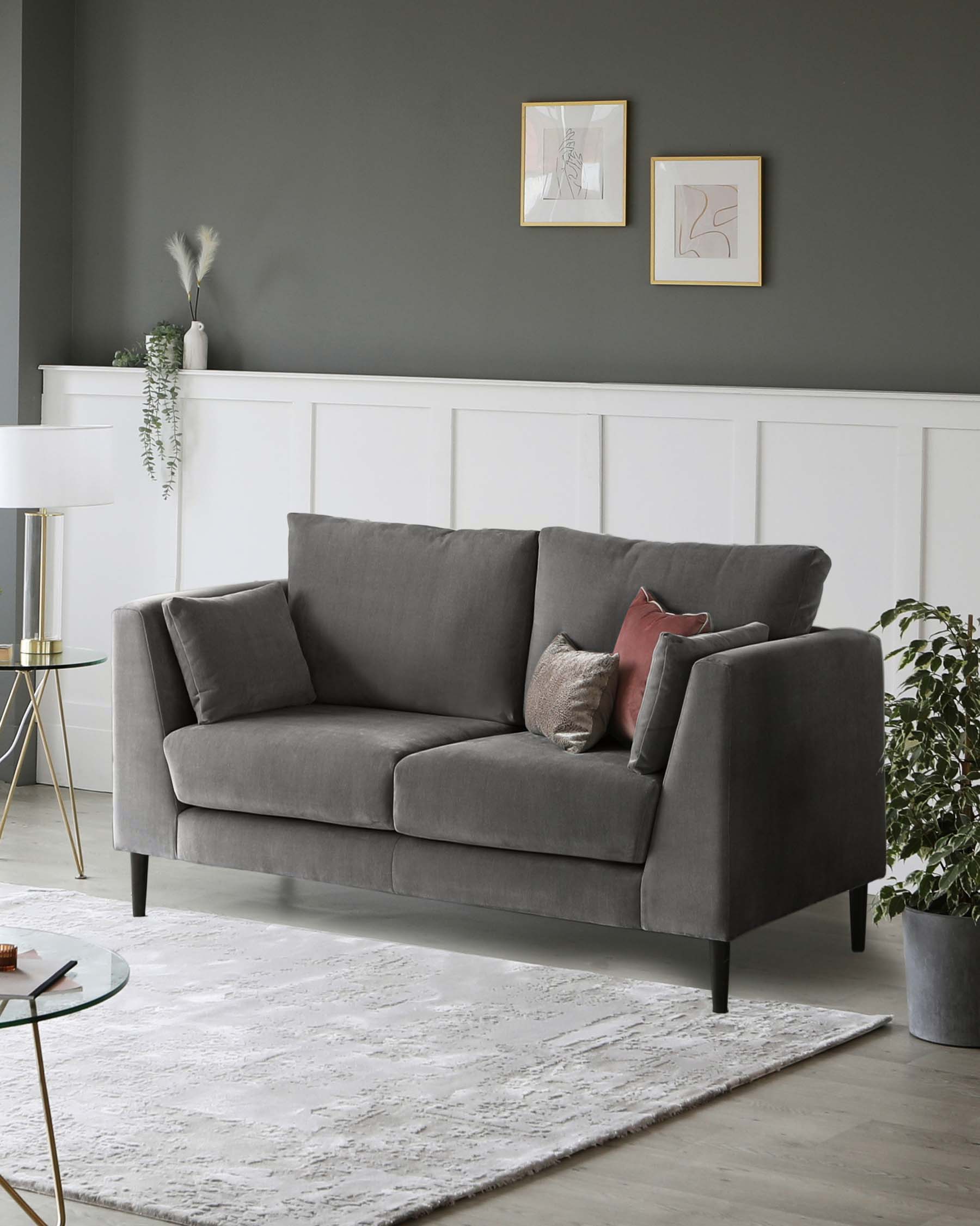 Elegant contemporary style living room featuring a grey upholstered three-seater sofa with plush cushions. A round glass-top side table with a gold metal base to the left, and a white textured area rug underneath. The setting is complemented by a modern white floor lamp with a gold accent, adding a touch of luxury to the space.