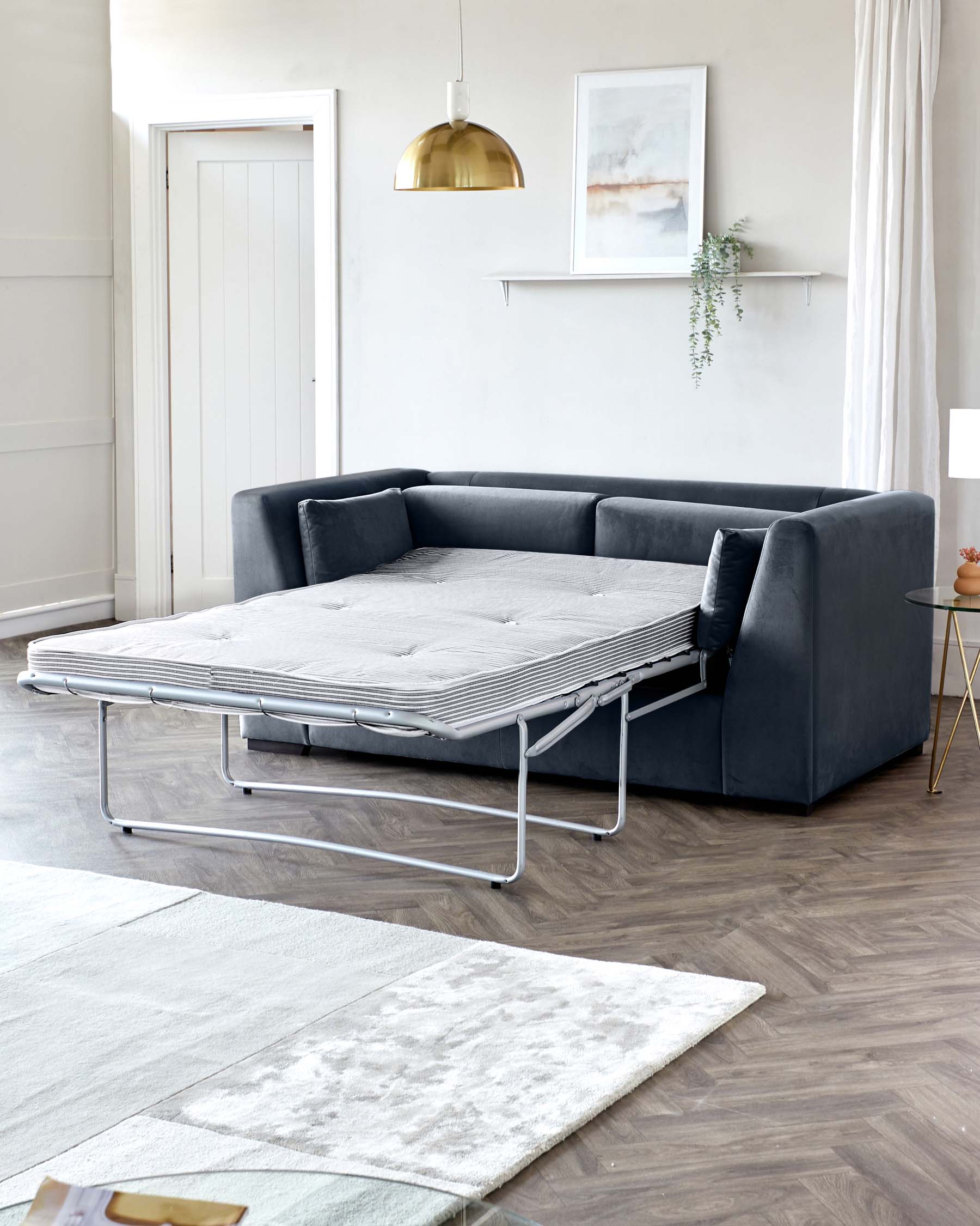 Elegant dark grey corner sofa with a sleek, modern design, paired with a versatile sofa bed with a metallic frame extended in the foreground. A plush, tufted mattress pad atop the sofa bed adds comfort and style. The setup is complemented by a soft, patterned area rug partially underneath the bed.