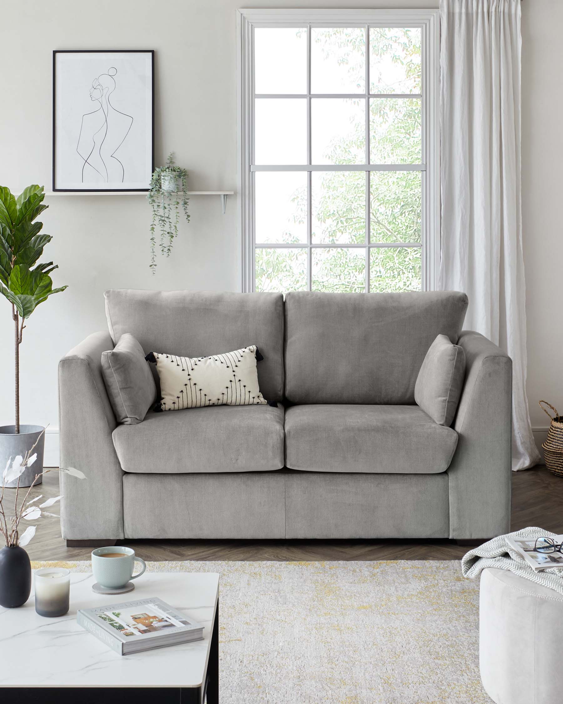 A modern three-seater sofa upholstered in light grey fabric, featuring plush cushions, simple arms, and clean lines. Accompanied by a white marble top coffee table with a black metal frame, over a textured cream and yellow area rug. A white ottoman with a soft-looking fabric is partially visible in the foreground.