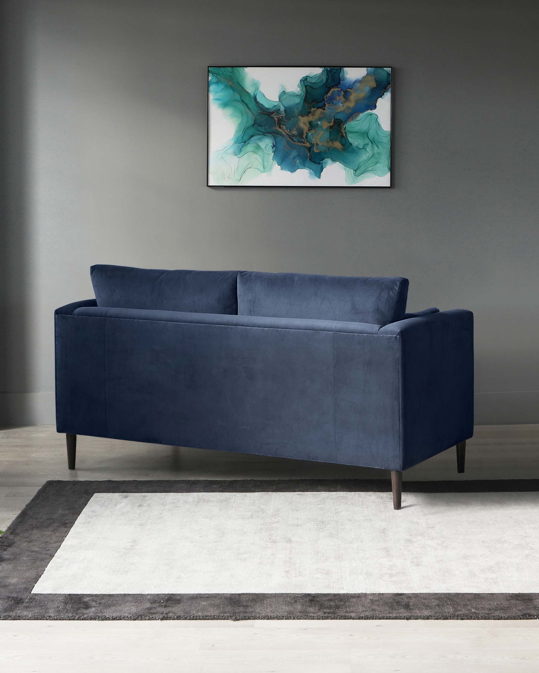 Elegant navy blue velvet loveseat with straight clean lines and dark wooden legs, placed on a two-tone grey and white area rug.