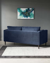 Navy blue three-seater sofa with a plush velvet upholstery and clean, modern lines, featuring dark wooden legs. The sofa is positioned on a two-tone grey area rug with a lighter central panel and darker border.