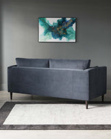 A contemporary charcoal grey velvet sofa with a streamlined silhouette and dark wooden legs, accompanied by a two-tone grey area rug on a wooden floor.