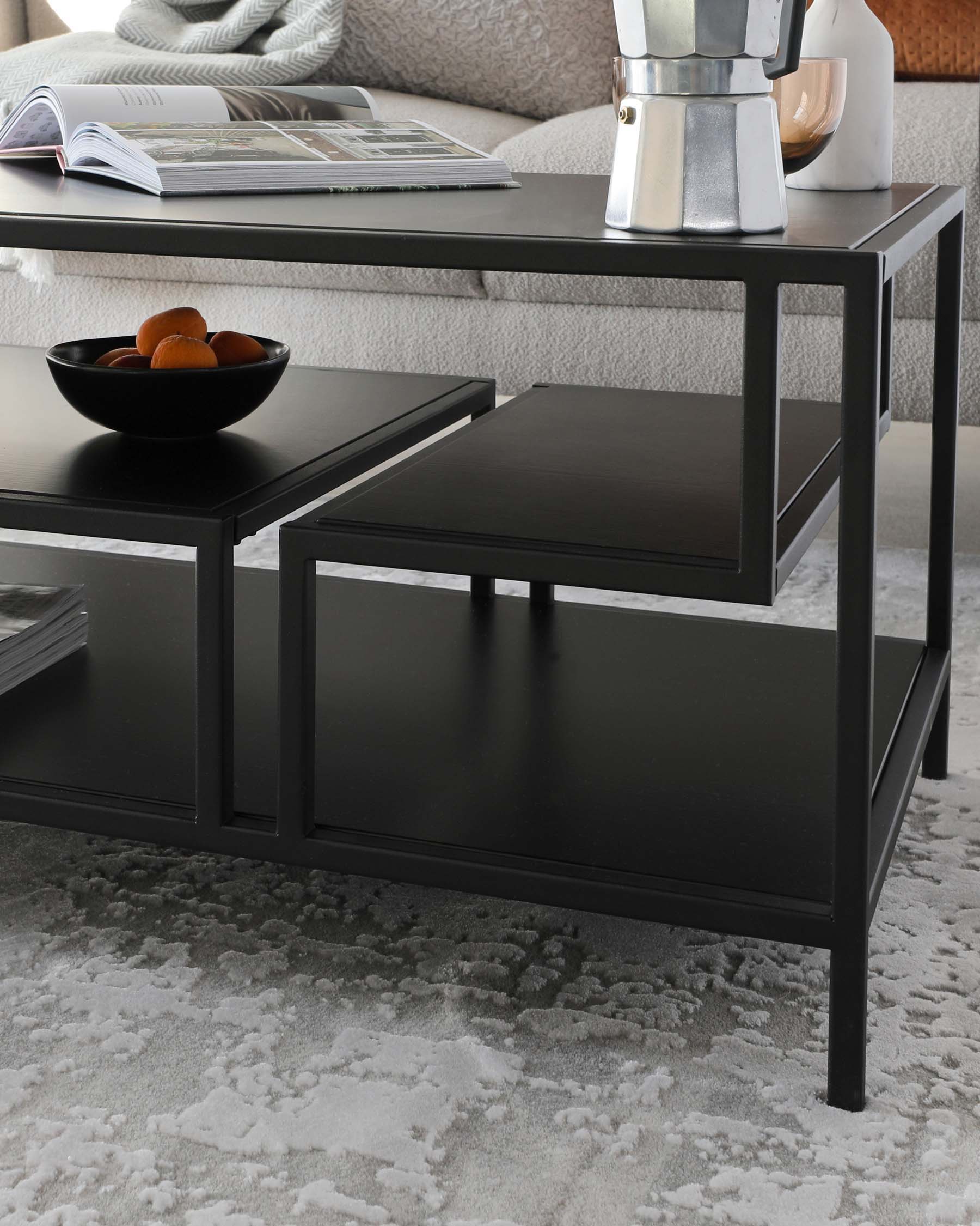 A contemporary, black metal coffee table with a rectangular top and a smaller square table nested underneath it. The sleek design features straight lines and a minimalist look, with a bowl of oranges and a coffee maker perched on top of it. Set on a plush grey rug, this furniture piece exudes a modern and chic aesthetic.