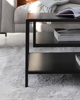 Modern black metal side table with a sleek rectangular shape, featuring two tiers for ample storage, set on a plush grey and white patterned area rug beside a grey upholstered couch with a cosy throw blanket.