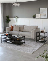 Modern living room showcasing a textured beige three-seater sofa adorned with assorted cushions, complemented by a sleek black coffee table with a rectangular top and lower shelves, paired with a matching side table, all arranged on a soft grey patterned area rug.