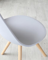 Modern minimalist chair with a matte white scoop seat and natural wooden legs on a light wooden floor.