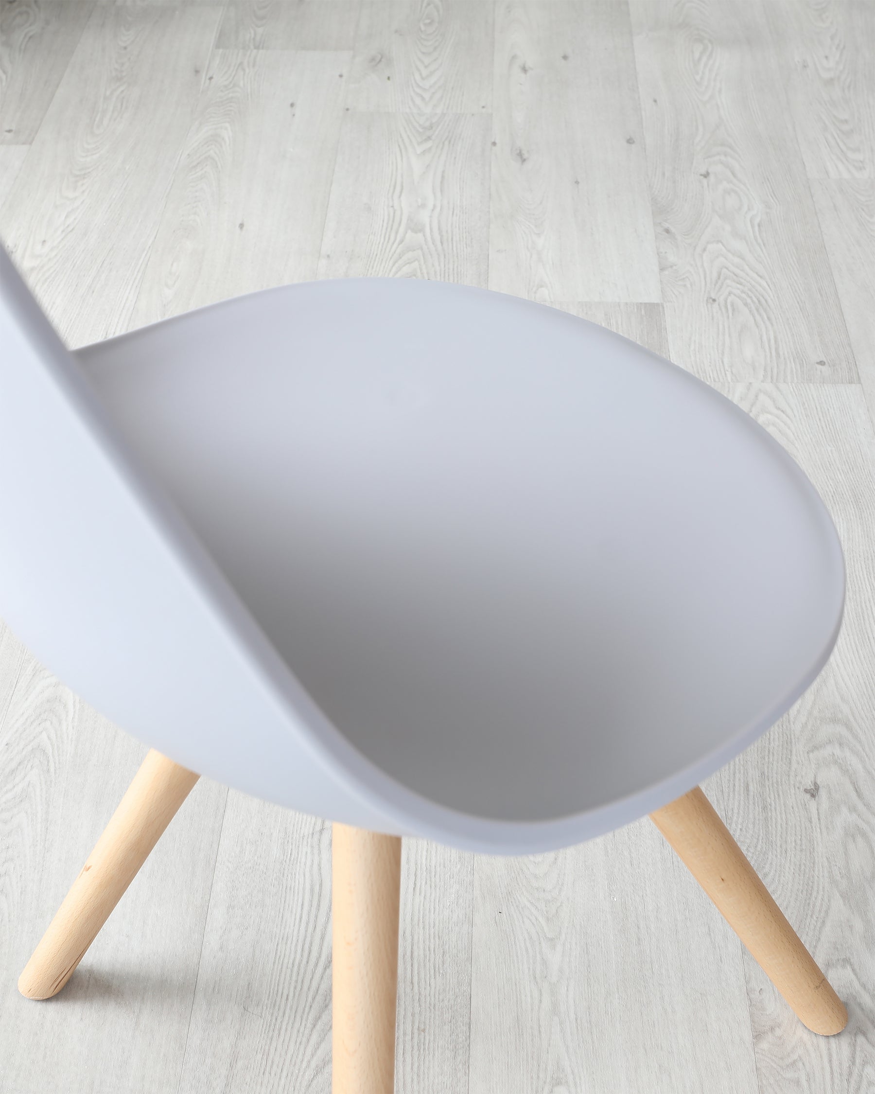 Modern minimalist chair with a matte white scoop seat and natural wooden legs on a light wooden floor.