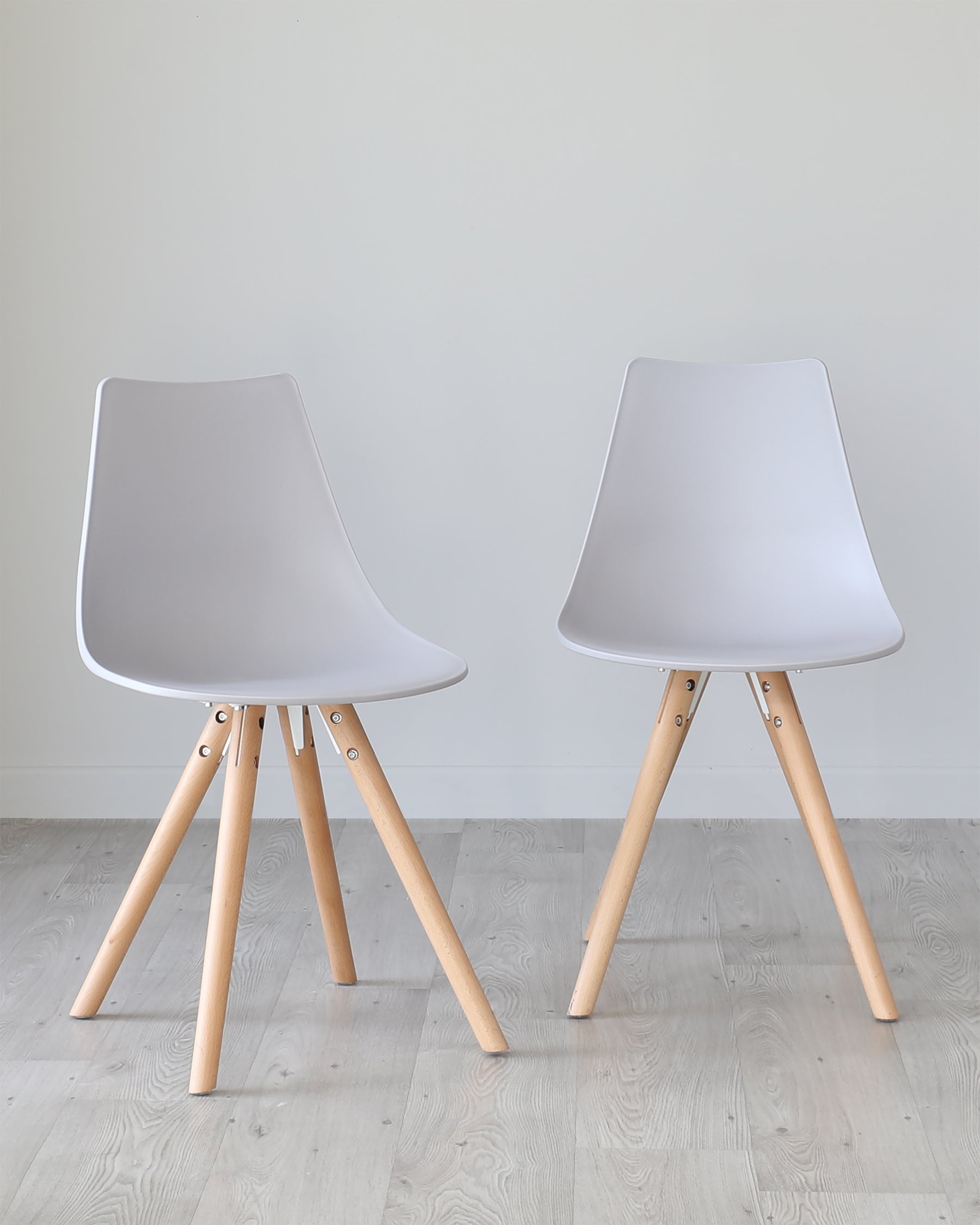 Two contemporary style chairs with matte grey plastic seats and light wooden legs angled outward, connected by black metal supports. The chairs are positioned on a light wood floor against a neutral grey background.