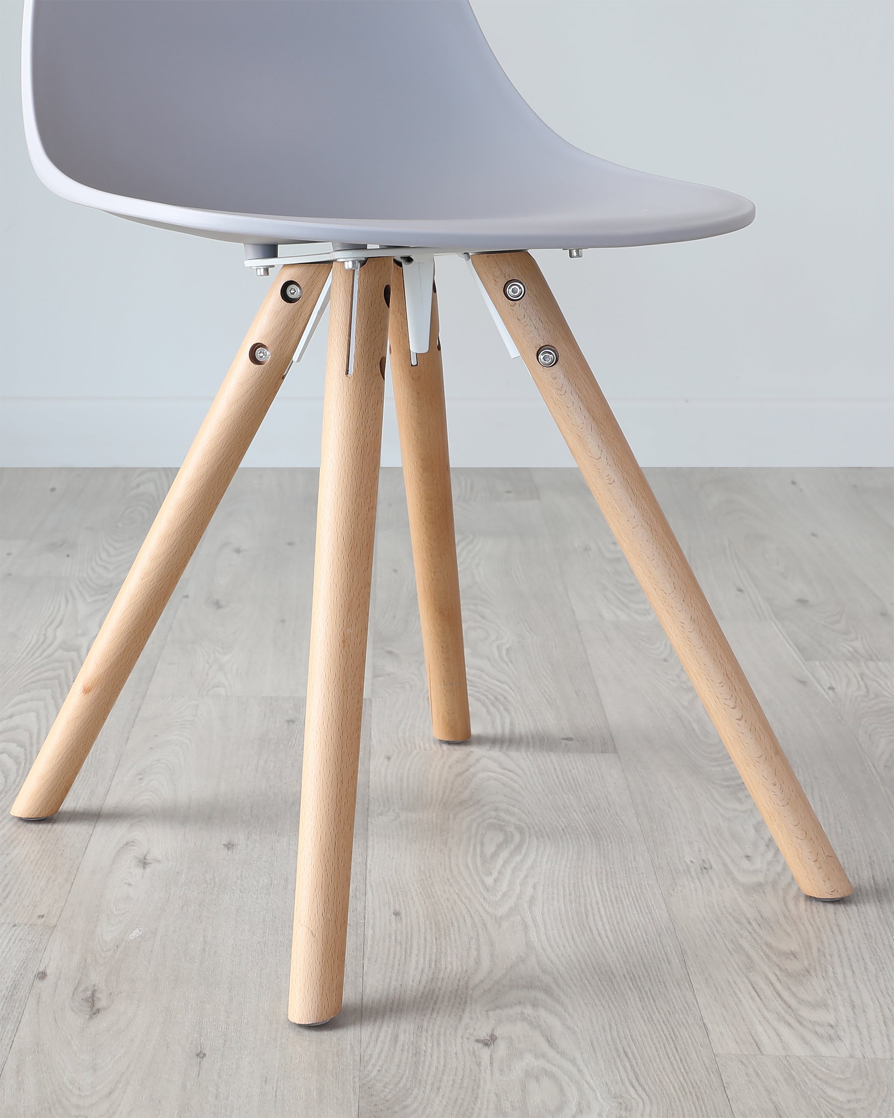 Modern minimalist chair with a white moulded shell and angled wooden legs, connected with black metal braces, against a light wood laminate floor.