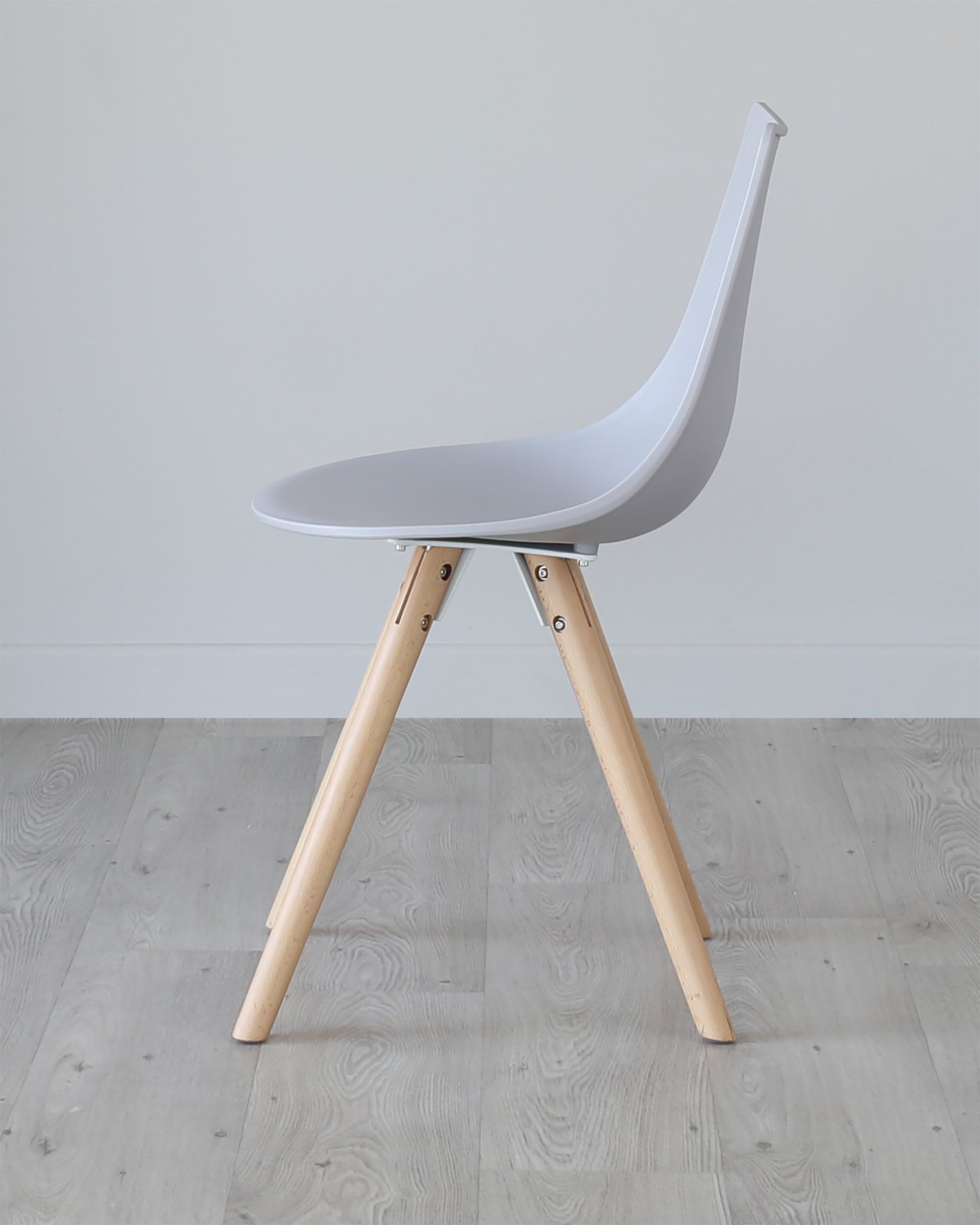 Modern minimalist chair with a white moulded plastic seat and natural wood legs, set against a grey floor and white wall background.