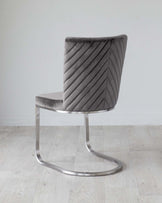 Modern velvet accent chair with a curved, high back and chevron pattern, plush grey upholstery, and a sleek, chrome-finished cantilever base.