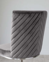 Modern grey velvet chair with a curved back featuring an elegant pleated design, set against a neutral background with a light wooden floor.