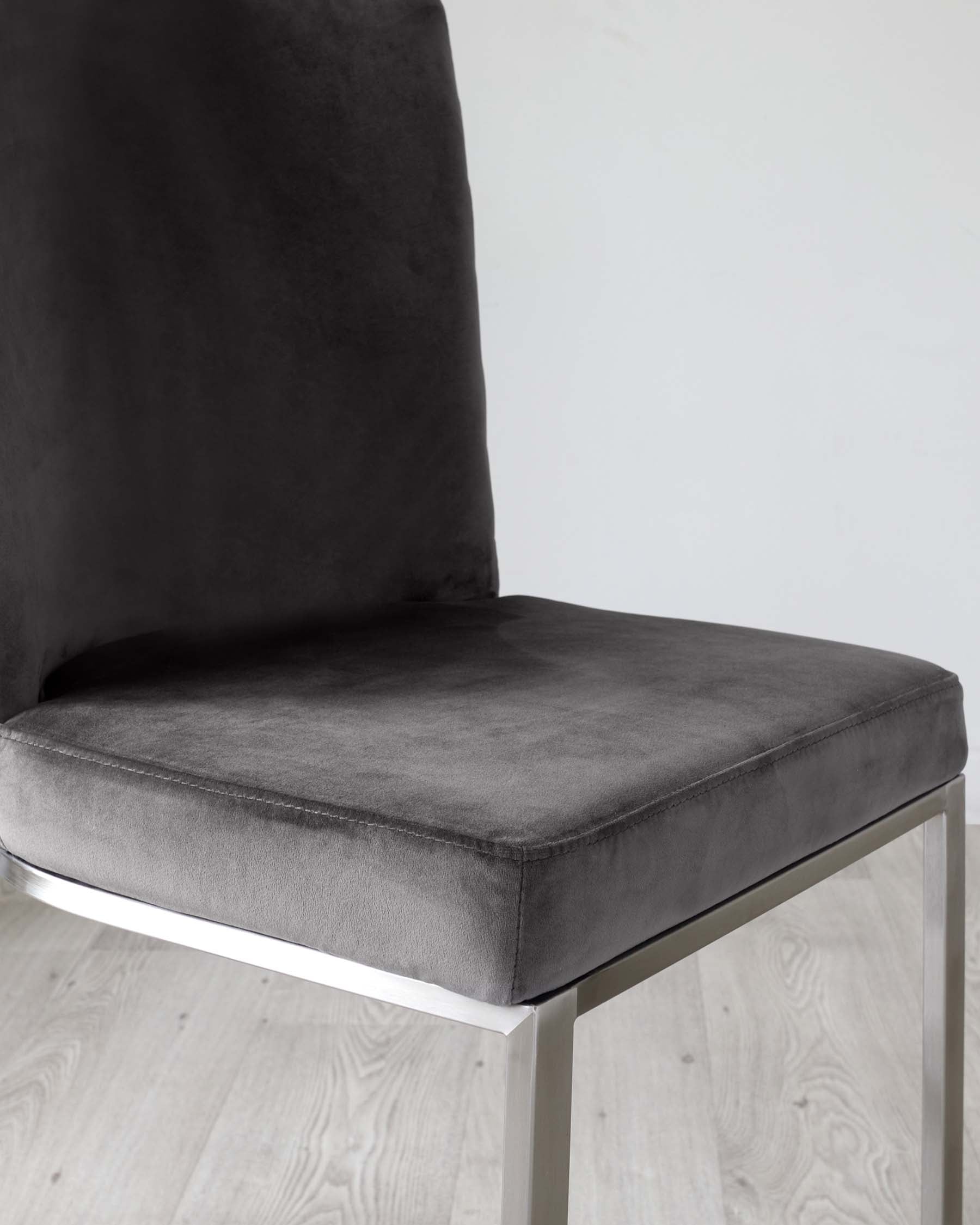 Modern chair with a sleek chrome frame and plush, dark grey upholstery, set against a light wooden floor and a white backdrop.