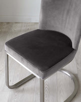 Modern low-back chair with a smooth, grey velvet upholstery and a sleek, silver metal base that forms a continuous, curved frame.