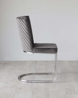 Modern grey velvet cantilever chair with vertical channel upholstery and a sleek, chrome base.