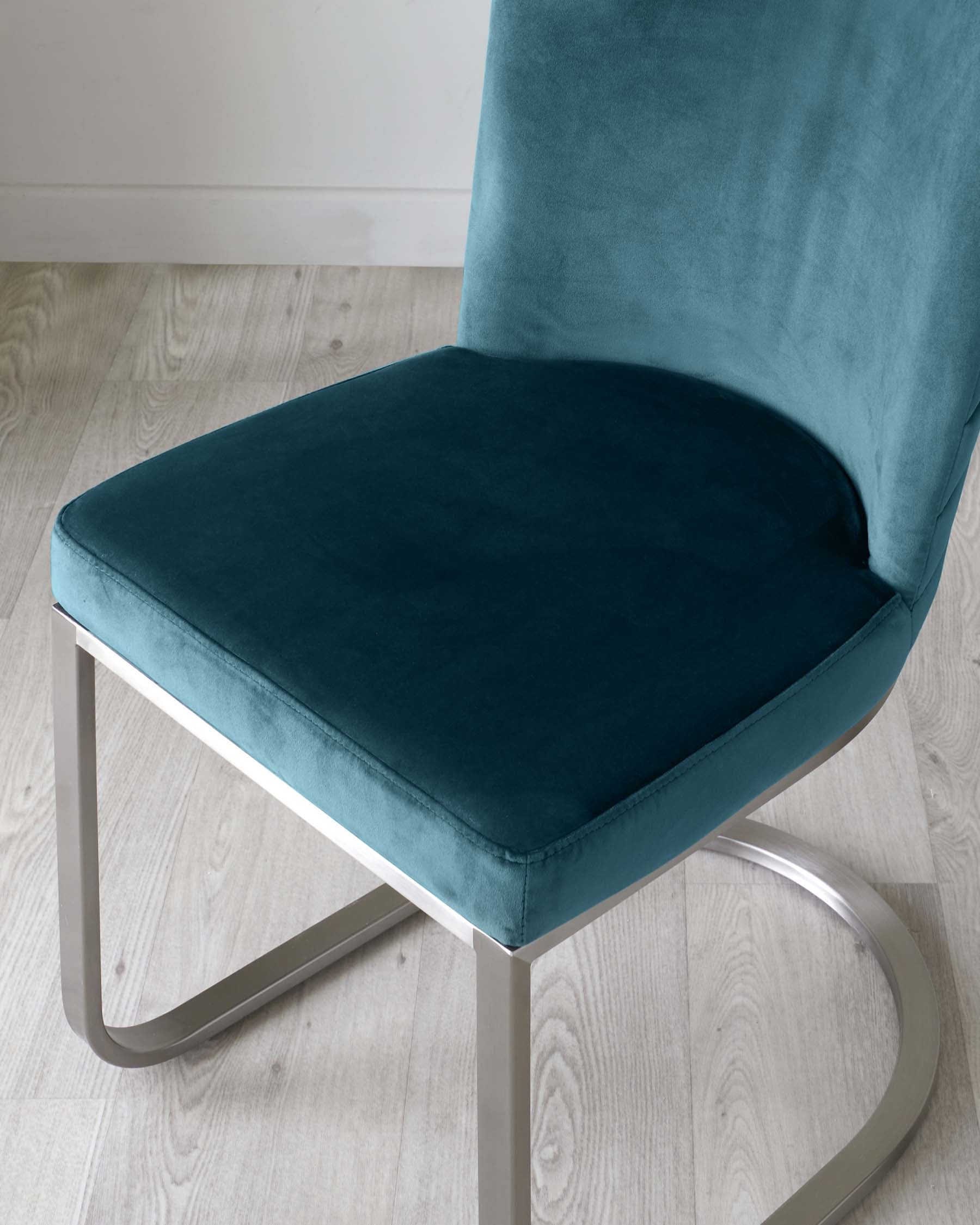 Modern teal velvet chair with a minimalist silver metal frame on a light wooden floor.