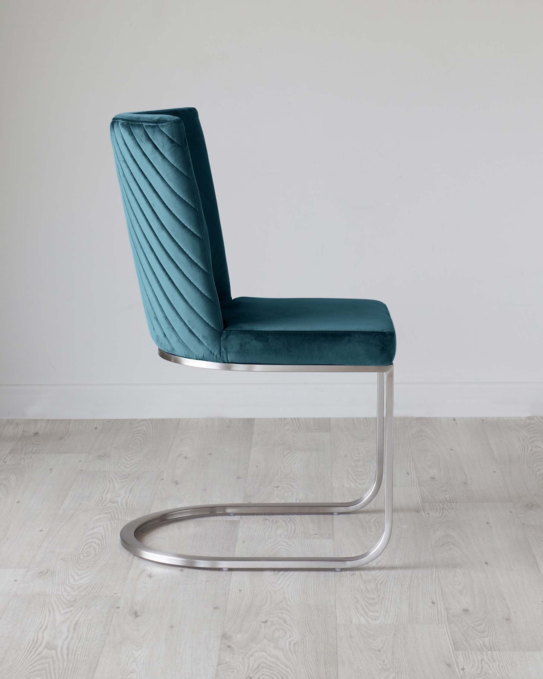 Modern teal velvet cantilever chair with a vertical channel-tufted backrest and sleek, chrome U-shaped base, displayed on a light wood floor against a white wall.