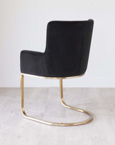 Modern black velvet accent chair with a sleek gold metal base in a cantilever design, featuring a high backrest and a smooth finish.