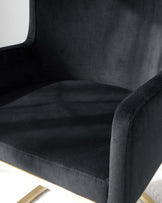 Elegant modern armchair with black velvet upholstery and a unique curved design, featuring a high-back seat and sleek metal legs in a brushed gold finish.