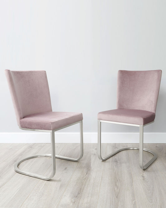 A pair of modern minimalist dining chairs with blush pink upholstery and sleek, cantilevered silver metal frames on a light wooden floor against a white wall.