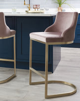 Luxurious velvet-upholstered bar stools with high backs and polished gold metal frame bases, in a contemporary kitchen setting with a navy blue island and brass accents.