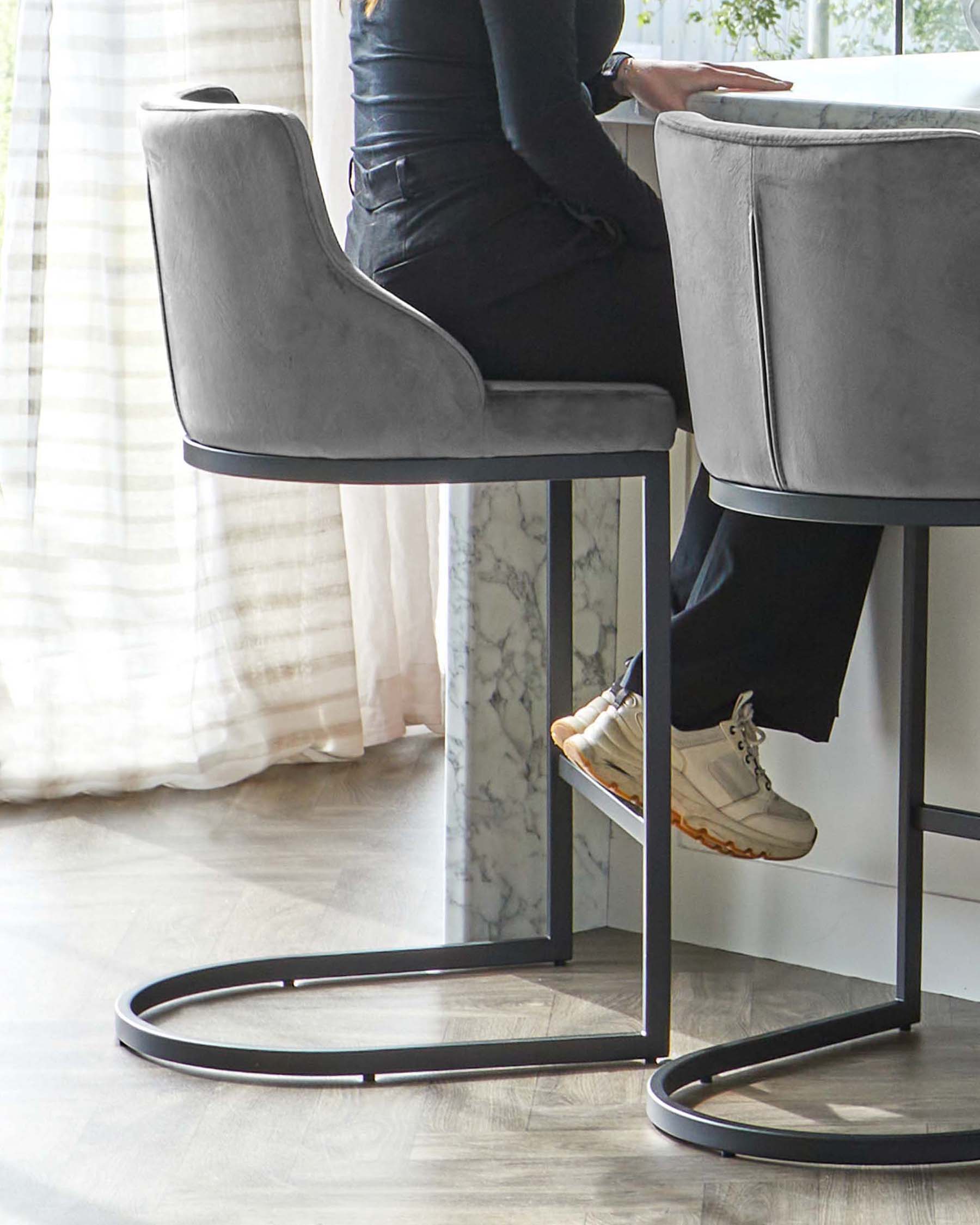 Elegant modern barstool with a high back and armrests, upholstered in grey velvet, featuring a sleek metal base with a circular footrest. The stool pairs with a white marble top bar table with a metal frame that complements the stool's design.