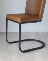 Modern minimalist dining chair with a caramel brown faux leather seat and backrest, mounted on a sleek black metal cantilever frame.