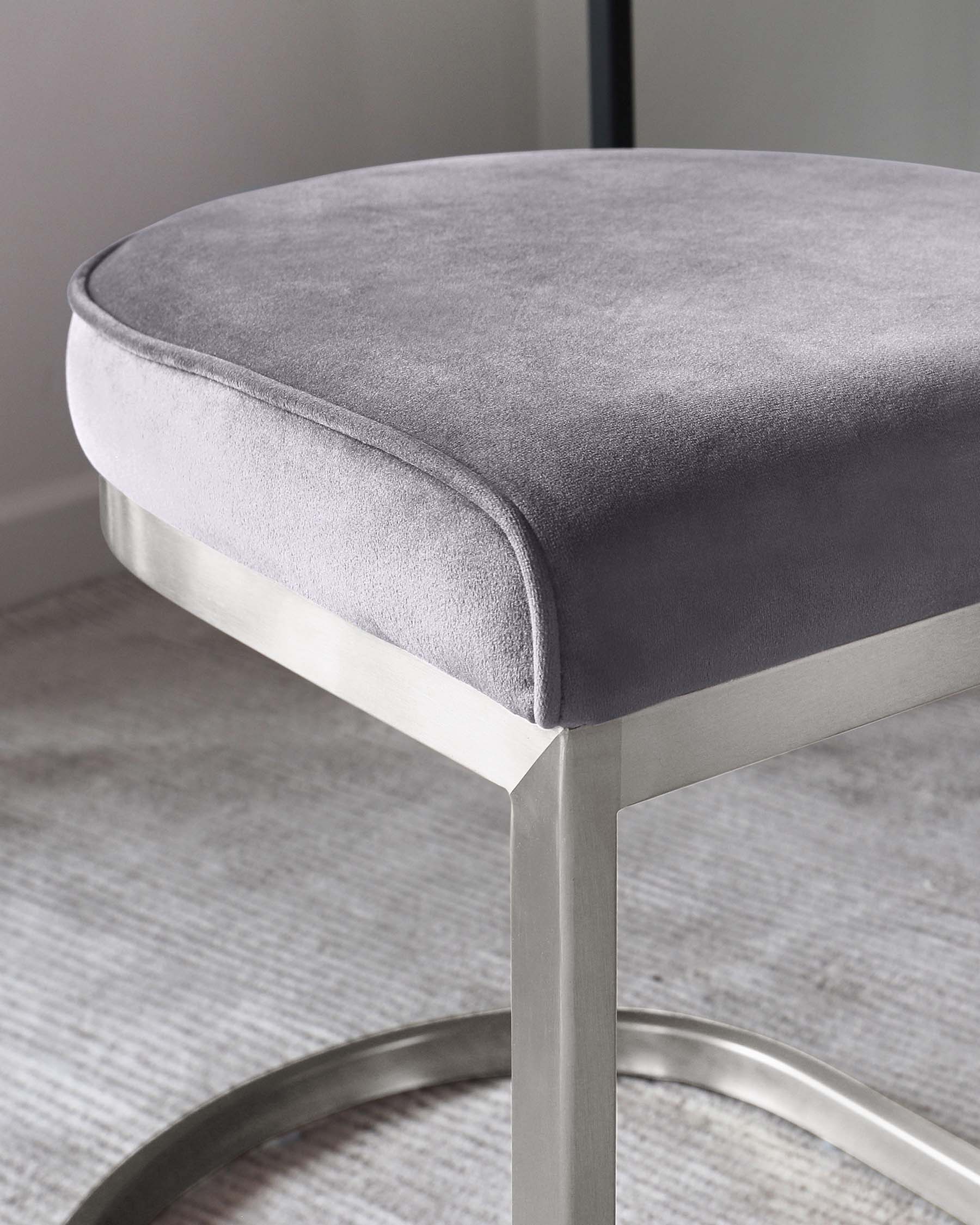 Modern round stool with a plush, grey velvet cushion and sleek metallic silver legs flaunting a gentle curve and a minimalist design.