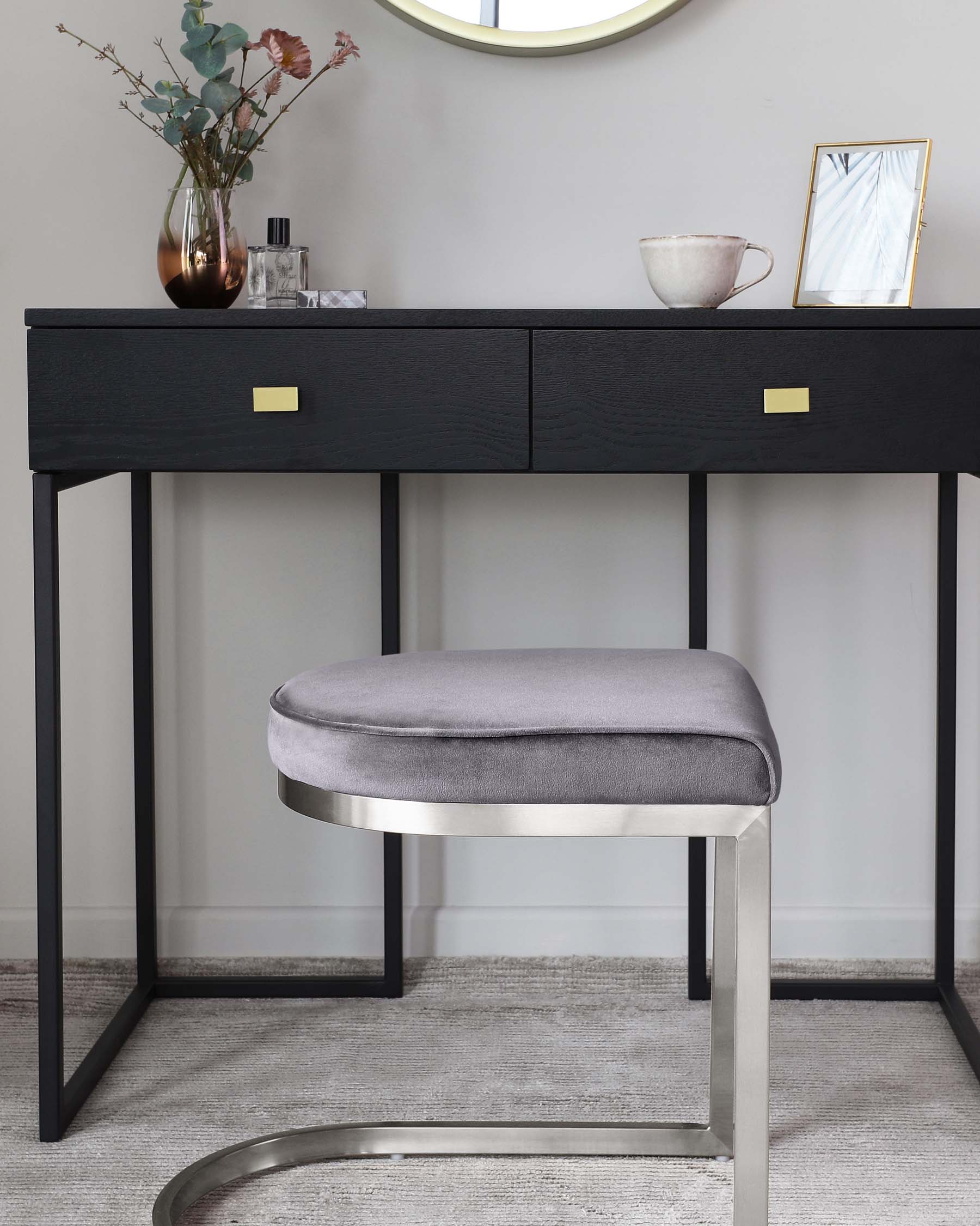 A modern, minimalist vanity table in black with sleek golden handles, paired with a round, padded stool upholstered in grey fabric, featuring a chic metallic base.